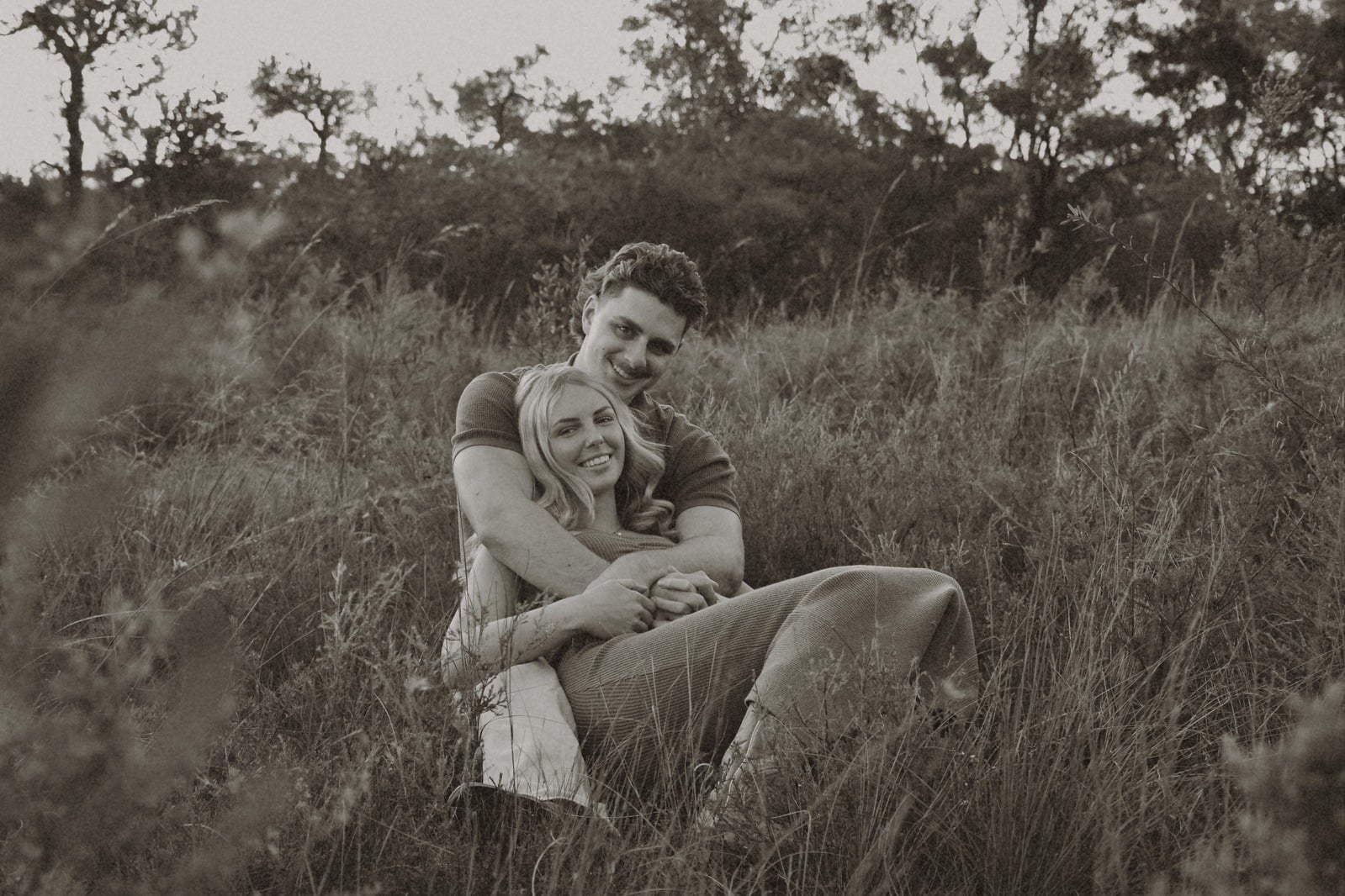 Couple sitting together in long grass at golden hour