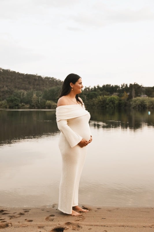 Expecting mother in a cream dress by the water